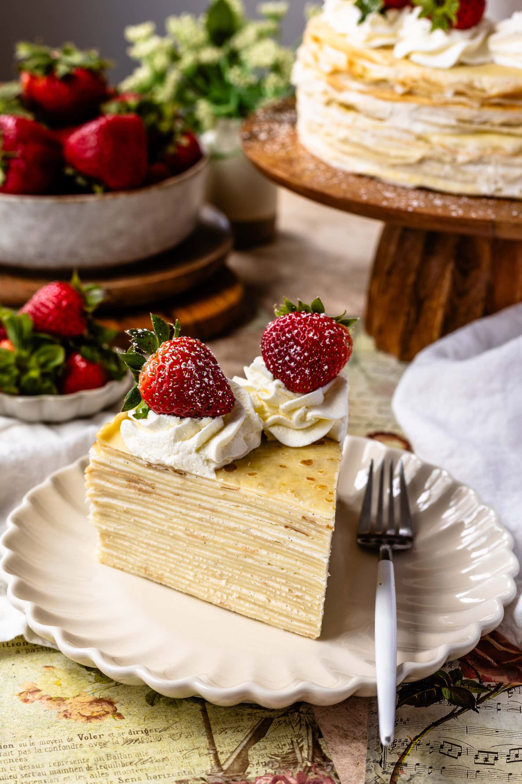slice of crepe cake on a plate with strawberries and whipped cream on top.