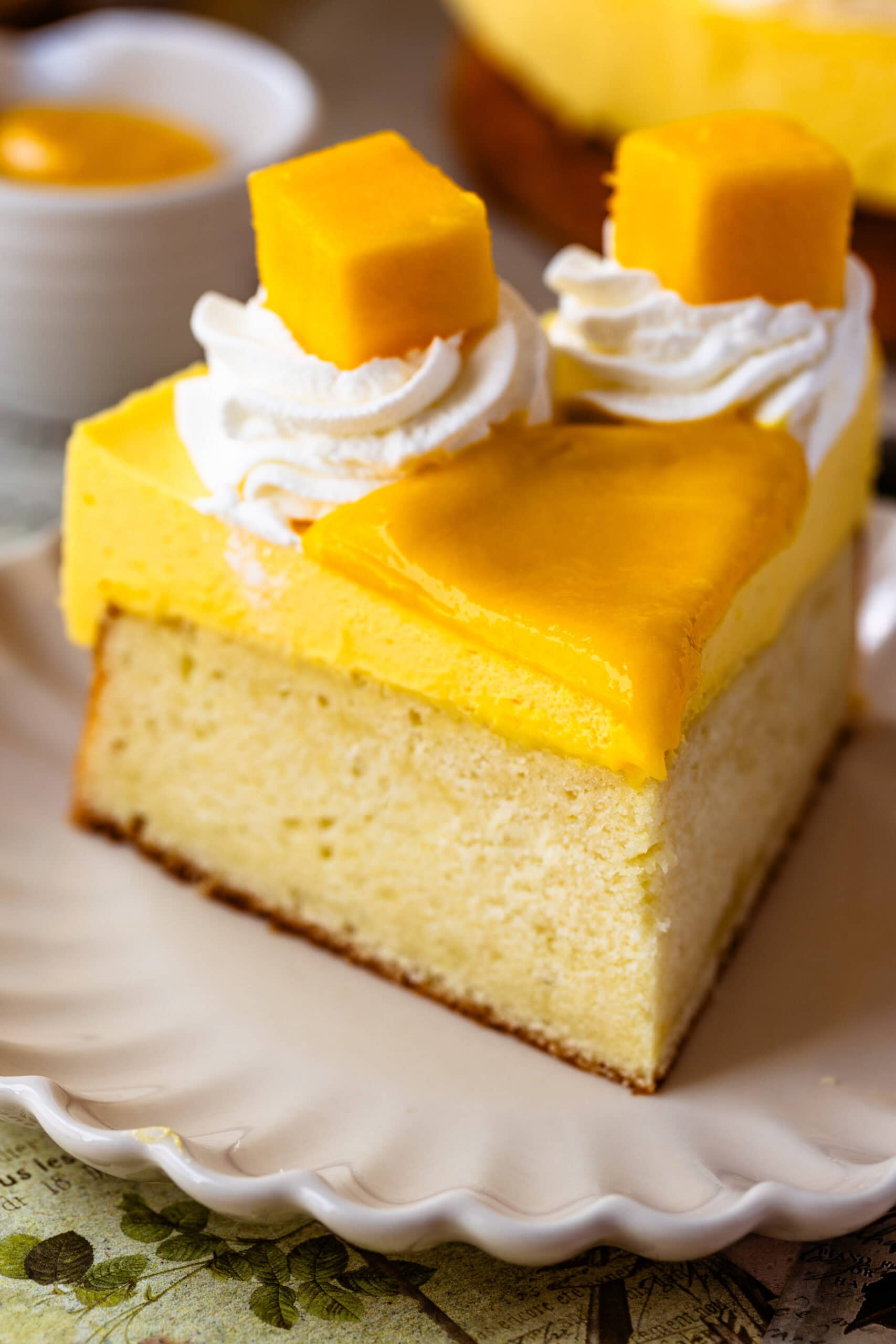 Mango Mousse Cake slice on a plate decorated with mango slices and whipped cream.