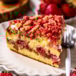slice of strawberry crunch cake on top of a plate, with a crunchy strawberry topping, and a strawberry filling.