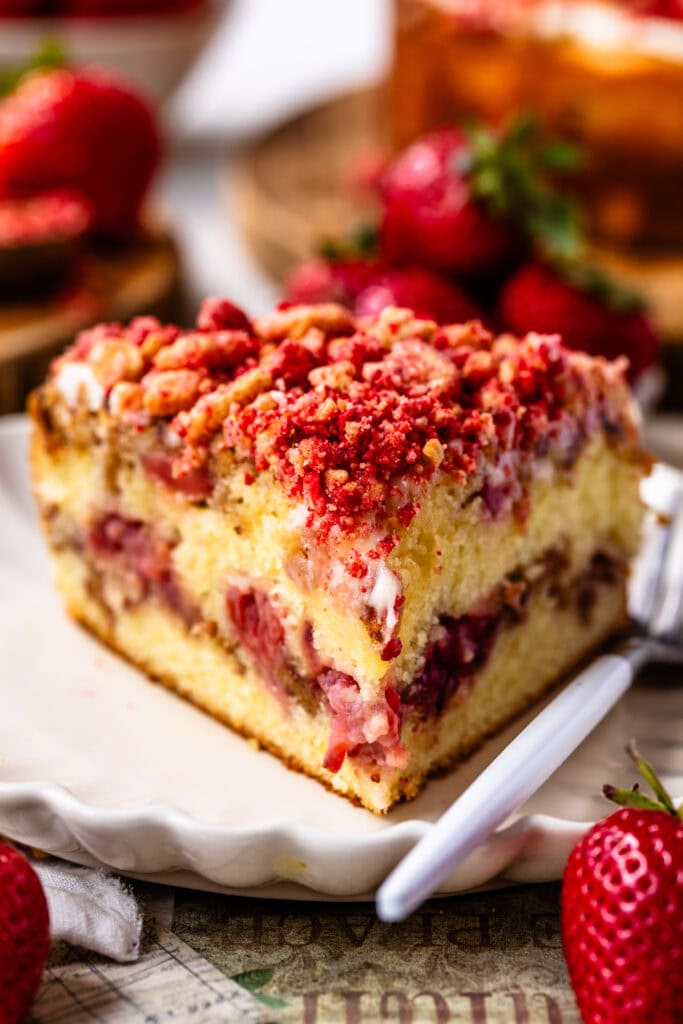 slice of strawberry crunch cake on top of a plate, with a crunchy strawberry topping, and a strawberry filling.