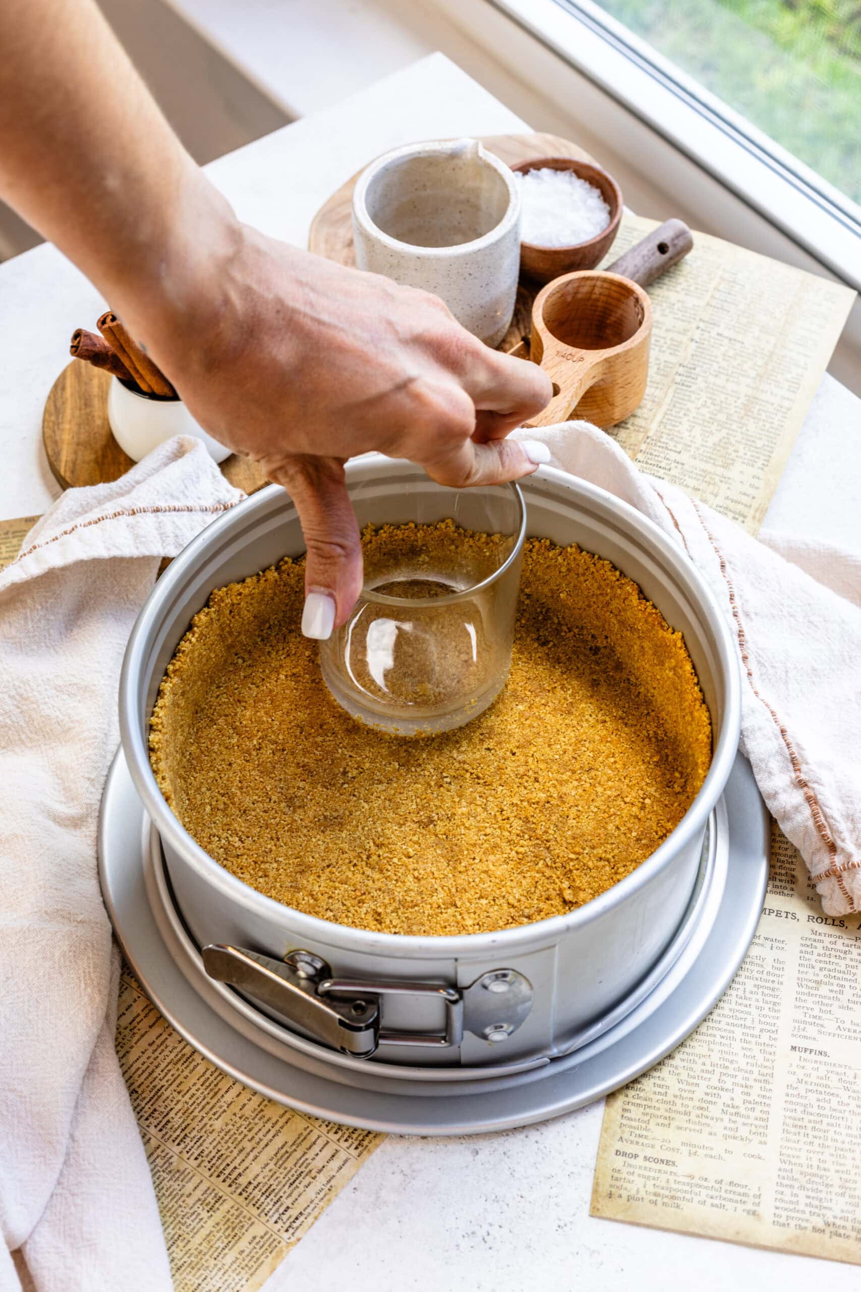 pressing graham cracker crust on the bottom of a cheesecake pan with a cup.