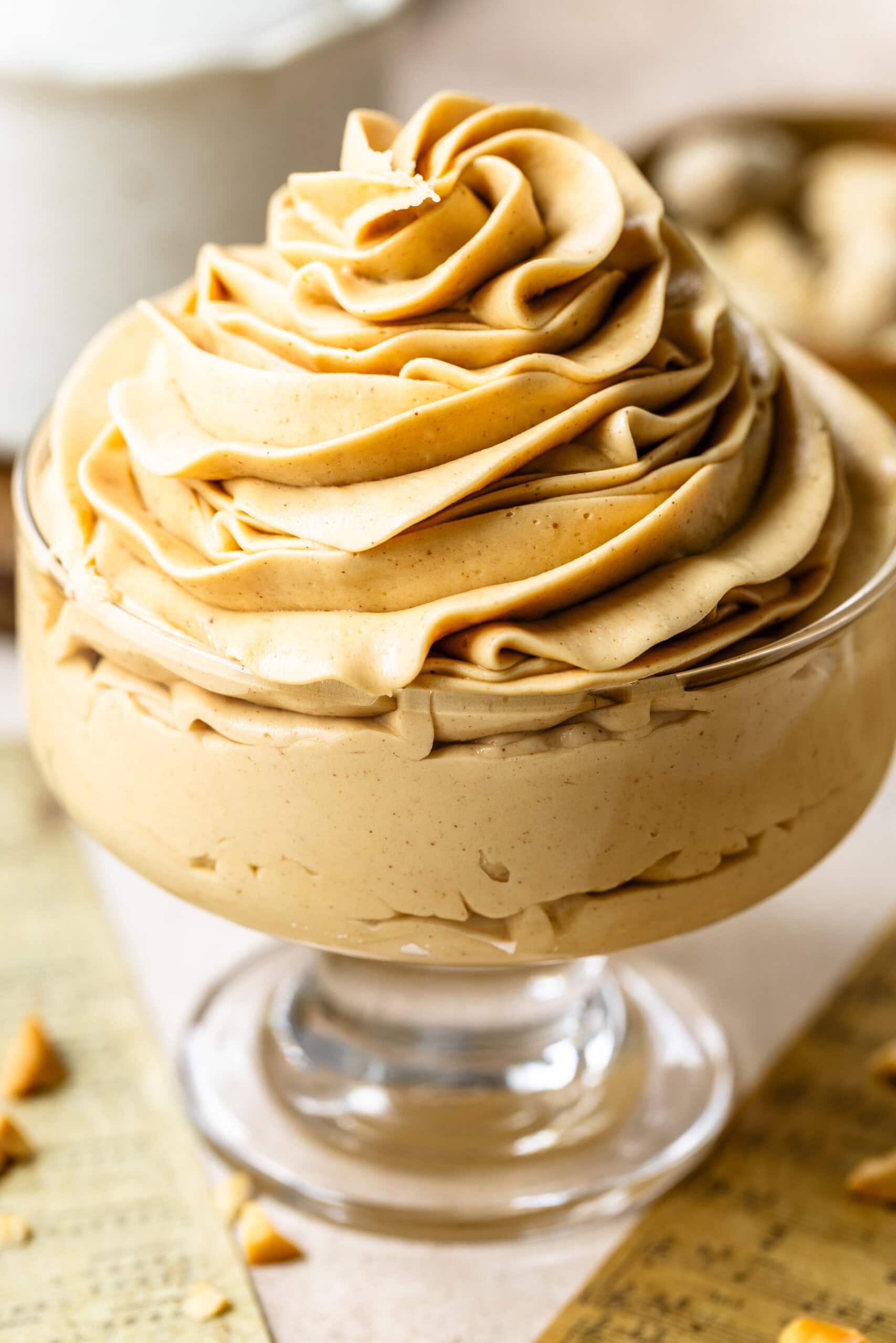 Peanut Butter Frosting Swirled in a Dish (Alternate Angle): Another close-up of the same glass dish filled with peanut butter frosting, taken from a slightly different angle. The frosting appears even more luscious, with its delicate swirls and rich, creamy consistency clearly visible. The soft focus on the background emphasizes the texture of the frosting.