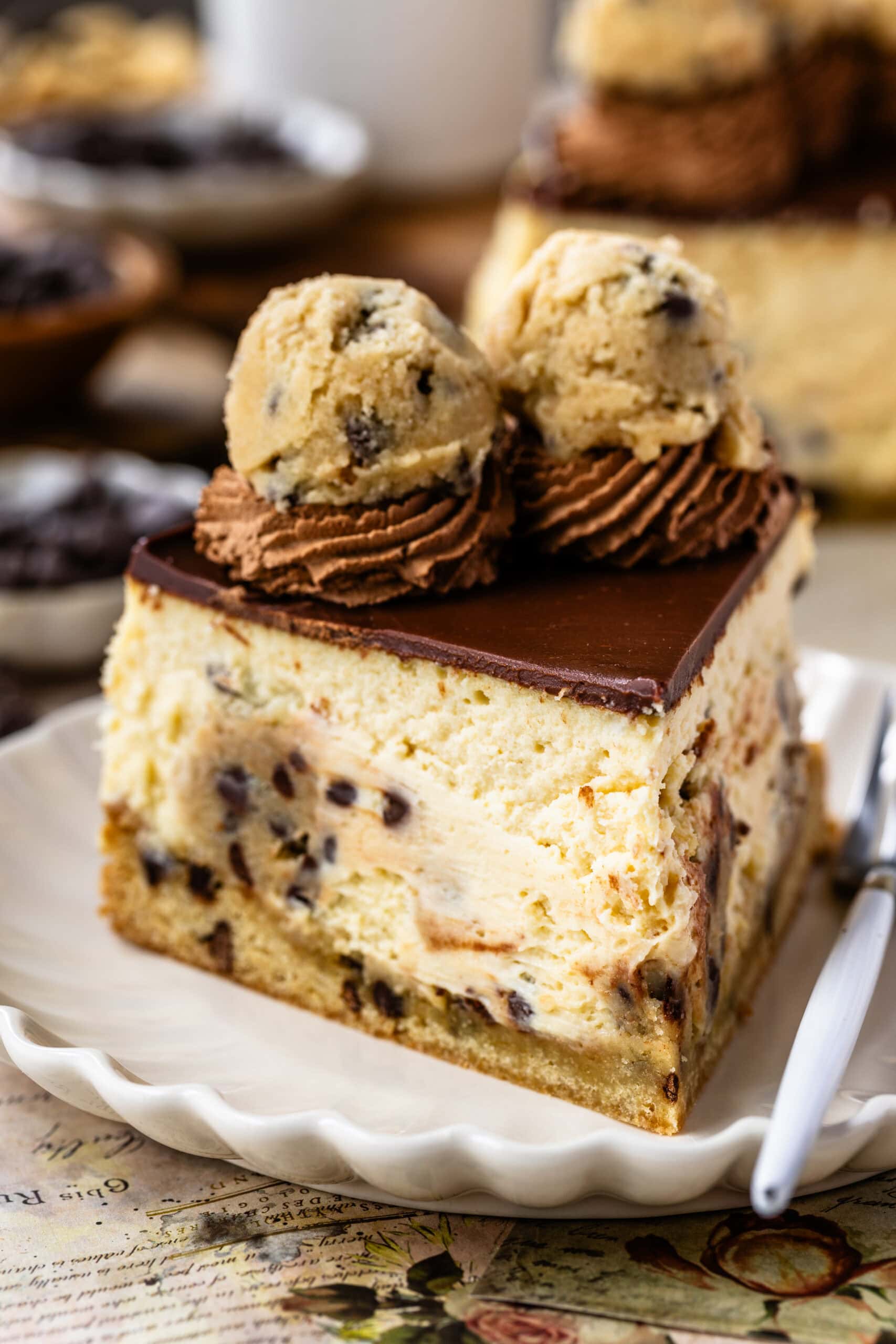 A close-up of a slice of cookie dough cheesecake, highlighting the creamy layers of cheesecake and cookie dough, topped with chocolate frosting swirls and cookie dough balls.