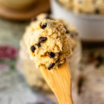 A close-up of a spoonful of edible cookie dough, loaded with chocolate chips, showcasing its creamy texture and perfect for snacking.