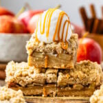 The image features a stack of golden apple crumb bars topped with a generous scoop of vanilla ice cream, drizzled with caramel sauce, adding an indulgent touch. The bars have a crunchy, crumbly top and reveal tender spiced apples nestled between the layers. The third image presents the bars neatly cut and arranged on a parchment-lined wooden board, highlighting their even, golden-brown crust. Surrounding the bars are apples, cinnamon sticks, and brown sugar, emphasizing the warm, autumnal flavors of the dessert.