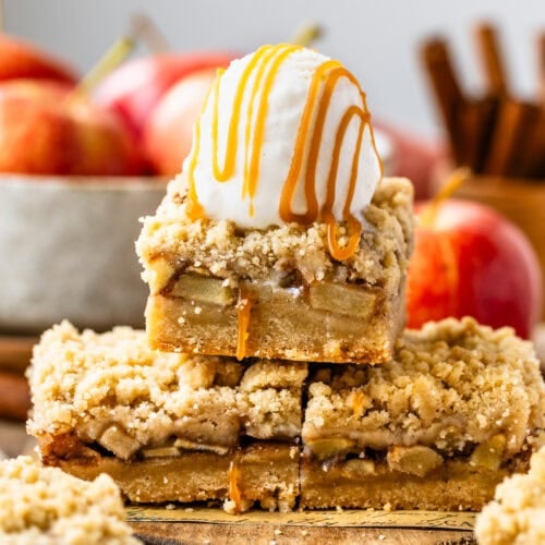 The image features a stack of golden apple crumb bars topped with a generous scoop of vanilla ice cream, drizzled with caramel sauce, adding an indulgent touch. The bars have a crunchy, crumbly top and reveal tender spiced apples nestled between the layers. The third image presents the bars neatly cut and arranged on a parchment-lined wooden board, highlighting their even, golden-brown crust. Surrounding the bars are apples, cinnamon sticks, and brown sugar, emphasizing the warm, autumnal flavors of the dessert.