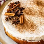 A chai spice cake topped with creamy frosting, dusted with cinnamon, and garnished with star anise and cinnamon sticks on a rustic plate.