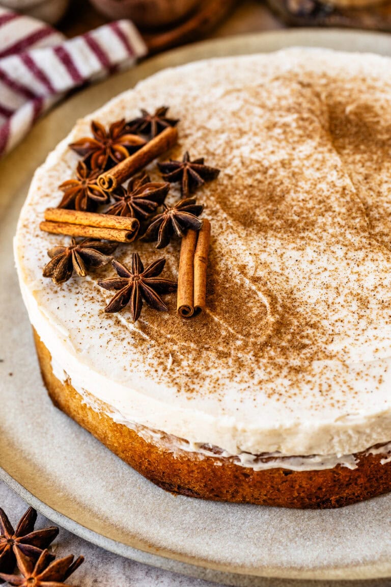 A chai spice cake topped with creamy frosting, dusted with cinnamon, and garnished with star anise and cinnamon sticks on a rustic plate.
