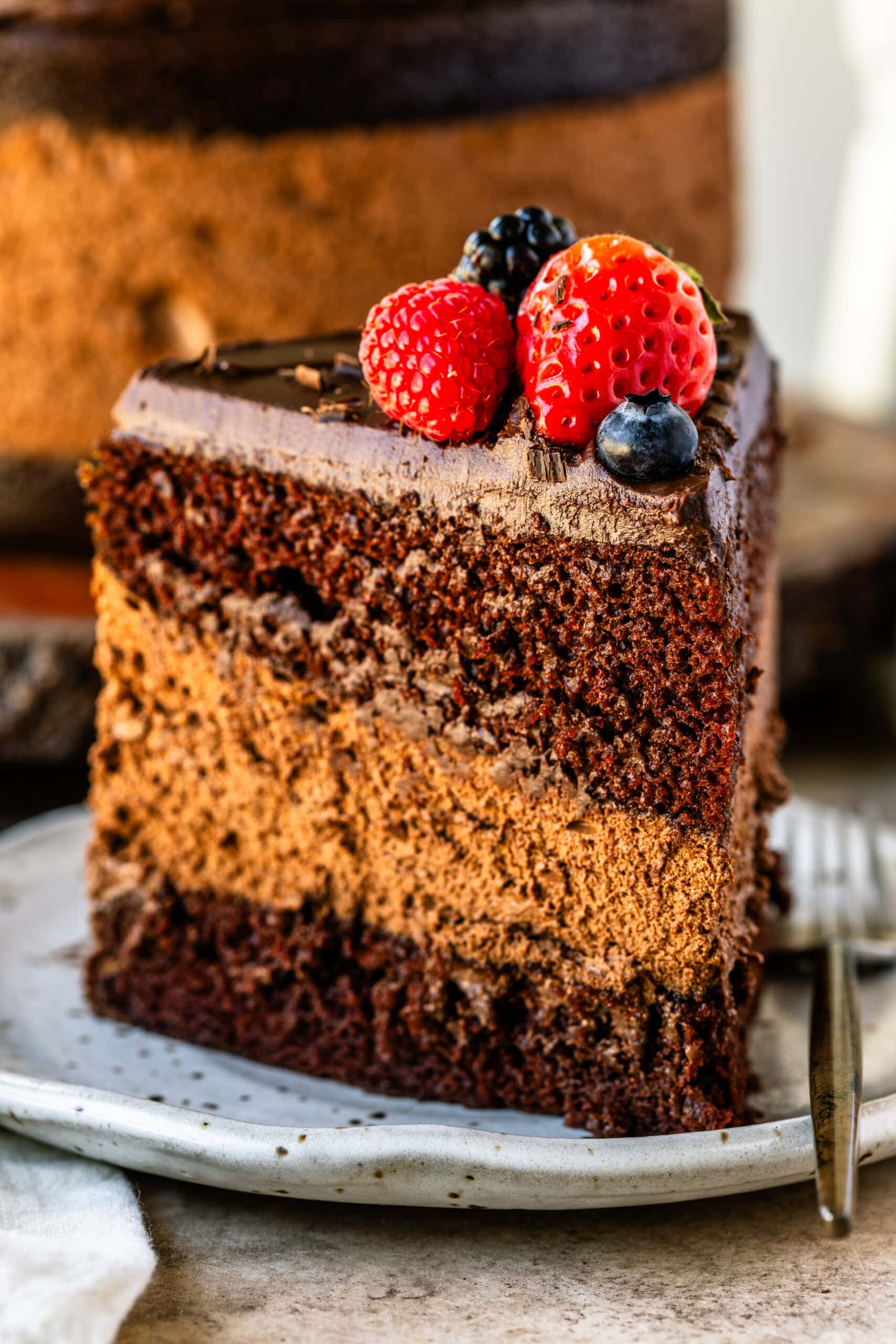 A slice of chocolate mousse cake on a plate, showcasing its rich layers of moist chocolate cake, creamy mousse, and smooth ganache, topped with fresh berries for a vibrant finish.