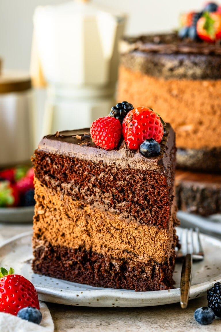 A slice of chocolate mousse cake on a plate, showcasing its rich layers of moist chocolate cake, creamy mousse, and smooth ganache, topped with fresh berries for a vibrant finish.