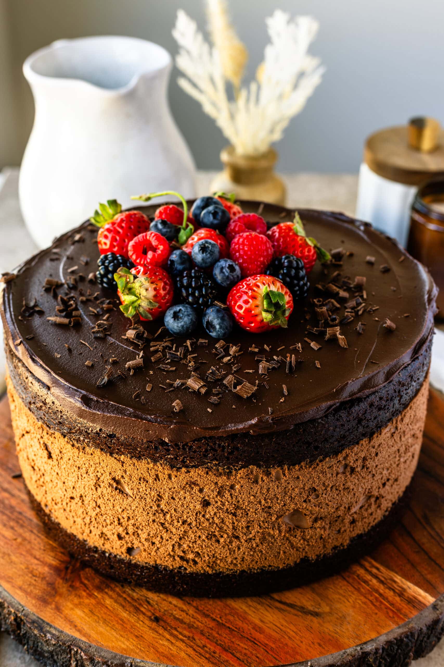 Decadent chocolate mousse cake with layers of rich chocolate topped with fresh berries and chocolate shavings, served on a rustic wooden board.
