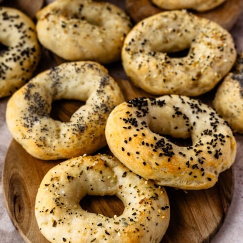Freshly baked high-protein bagels sprinkled with an assortment of seeds, arranged on a wooden serving board with creamy spread in the background.