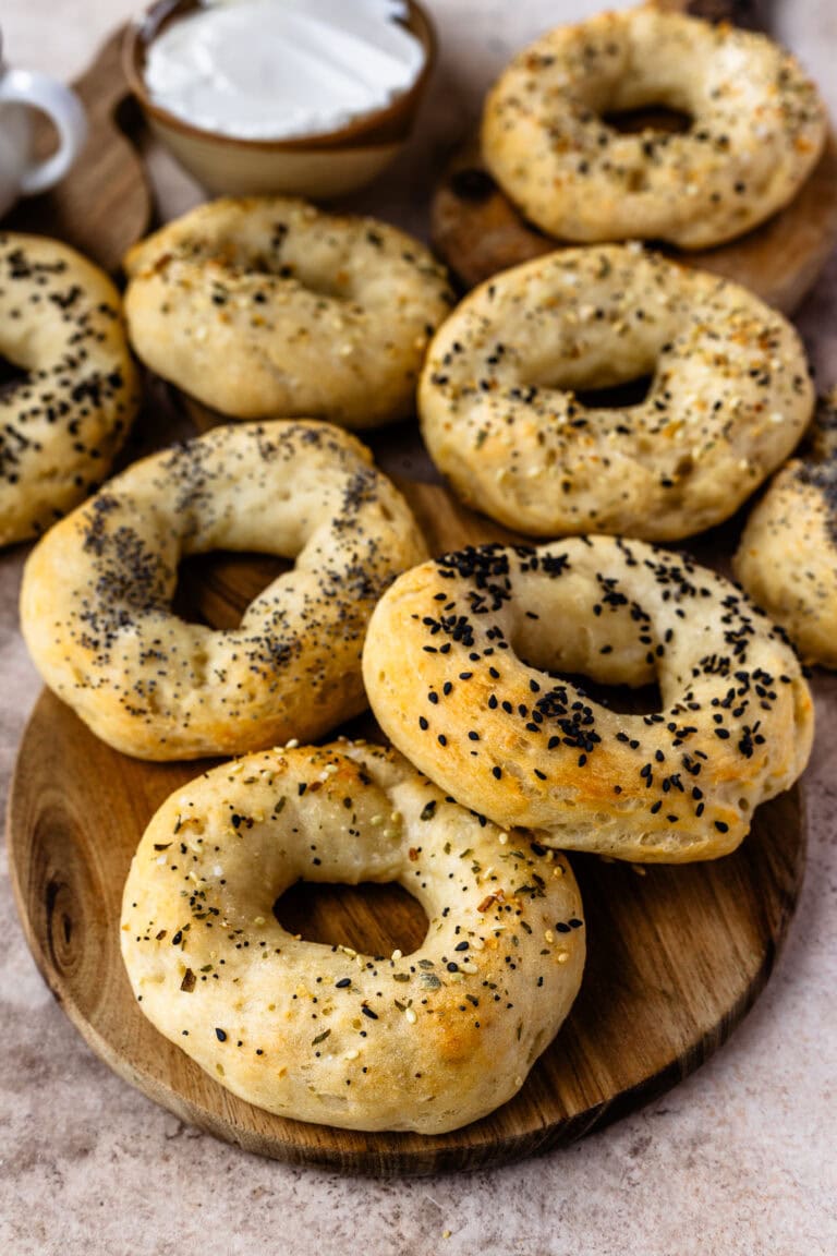 Freshly baked high-protein bagels sprinkled with an assortment of seeds, arranged on a wooden serving board with creamy spread in the background.