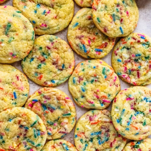 A batch of vibrant Funfetti cookies spread out on a surface, showcasing colorful sprinkles throughout, with a small bowl of rainbow sprinkles on the side.