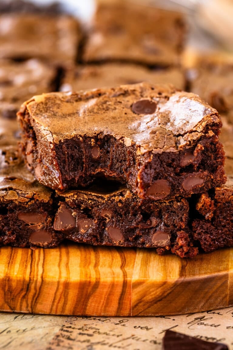 A close-up of two rich, fudgy brownies stacked on top of each other, with a bite taken from the top brownie, revealing a gooey chocolate interior and crackly tops.