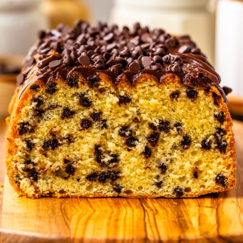 A close-up of a chocolate chip loaf cake topped with chocolate ganache and mini chips, sliced to reveal its soft, golden crumb and rich chocolate studding.