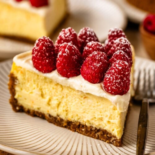 A slice of ricotta cheesecake topped with fresh raspberries and powdered sugar, served on a striped plate.