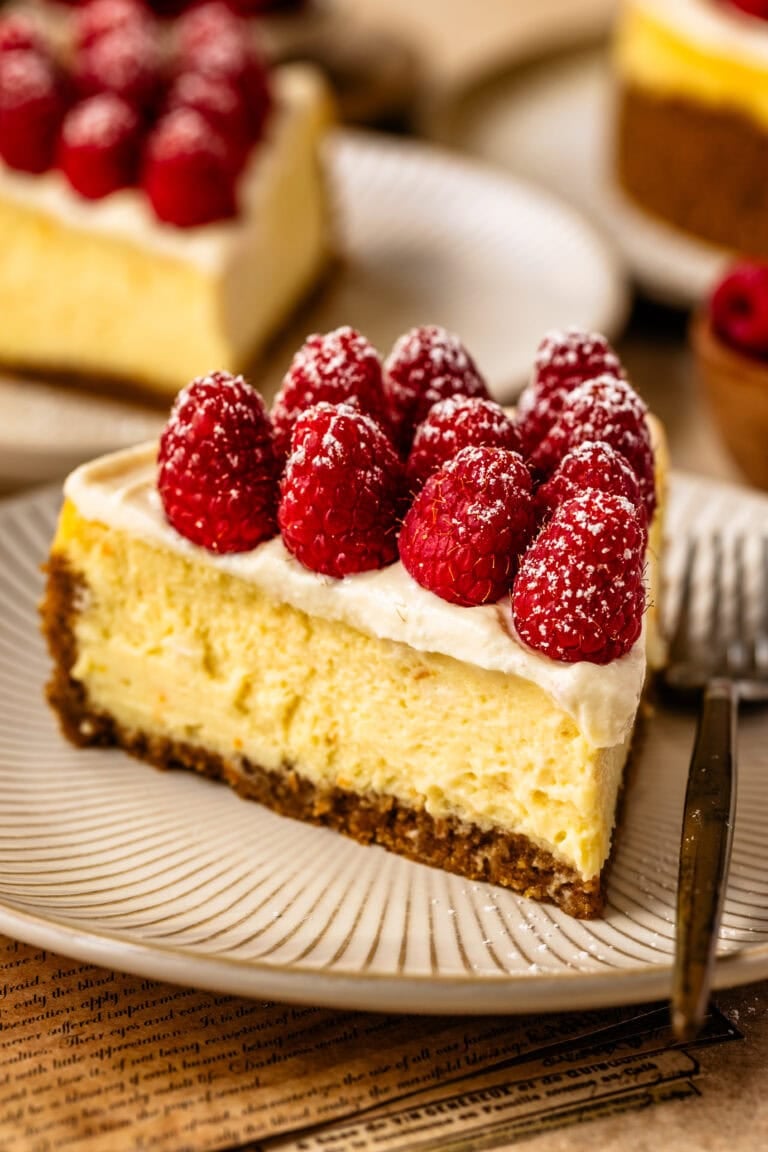 A slice of ricotta cheesecake topped with fresh raspberries and powdered sugar, served on a striped plate.