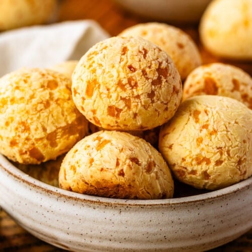 A close-up of pão de queijo in a rustic ceramic bowl, showing their golden, crackly tops and chewy texture.