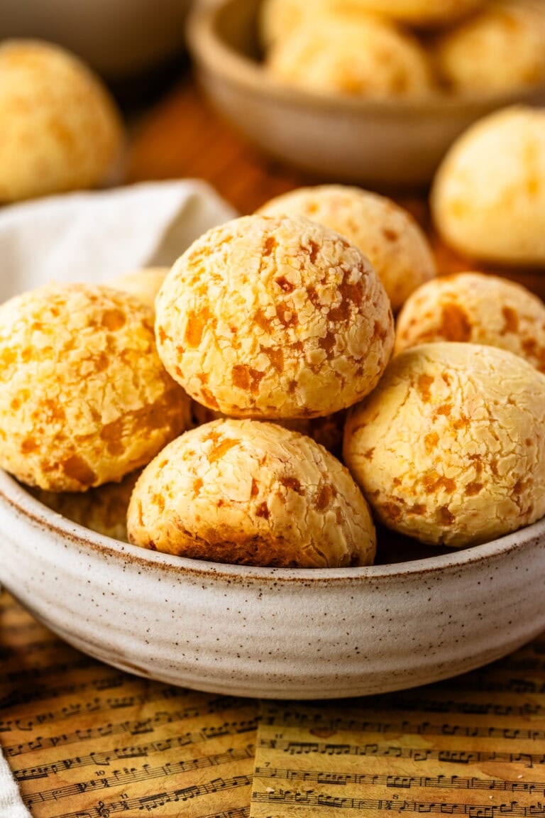 A close-up of pão de queijo in a rustic ceramic bowl, showing their golden, crackly tops and chewy texture.