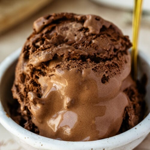 A dish of creamy homemade chocolate ice cream, scooped high in a glass dessert bowl with a spoon, slightly melting for the perfect just-scooped look.