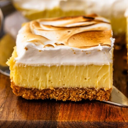 A close-up of a lemon meringue pie slice with a graham cracker crust, creamy lemon filling, and a thick layer of toasted meringue on top.