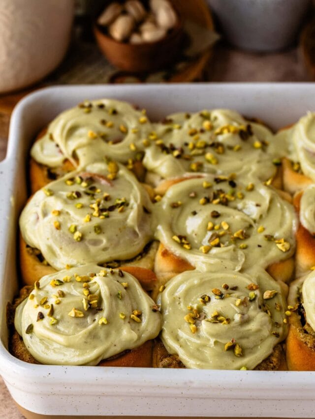 A pan of freshly baked pistachio rolls topped with creamy pistachio frosting and sprinkled with chopped pistachios.