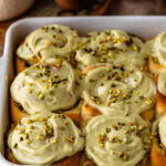 A pan of freshly baked pistachio rolls topped with creamy pistachio frosting and sprinkled with chopped pistachios.