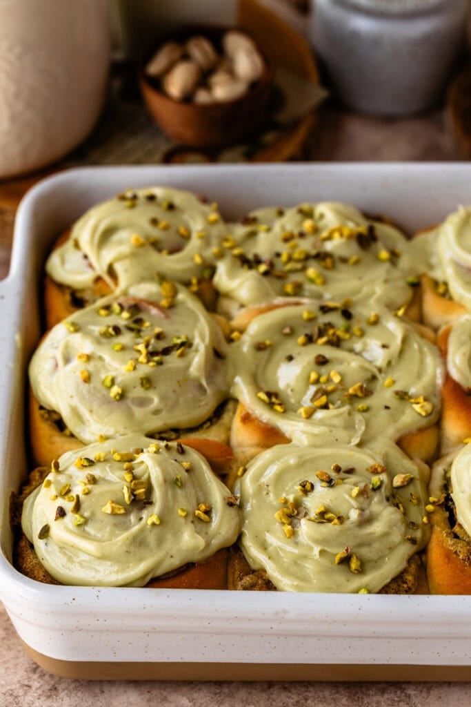 A pan of freshly baked pistachio rolls topped with creamy pistachio frosting and sprinkled with chopped pistachios.