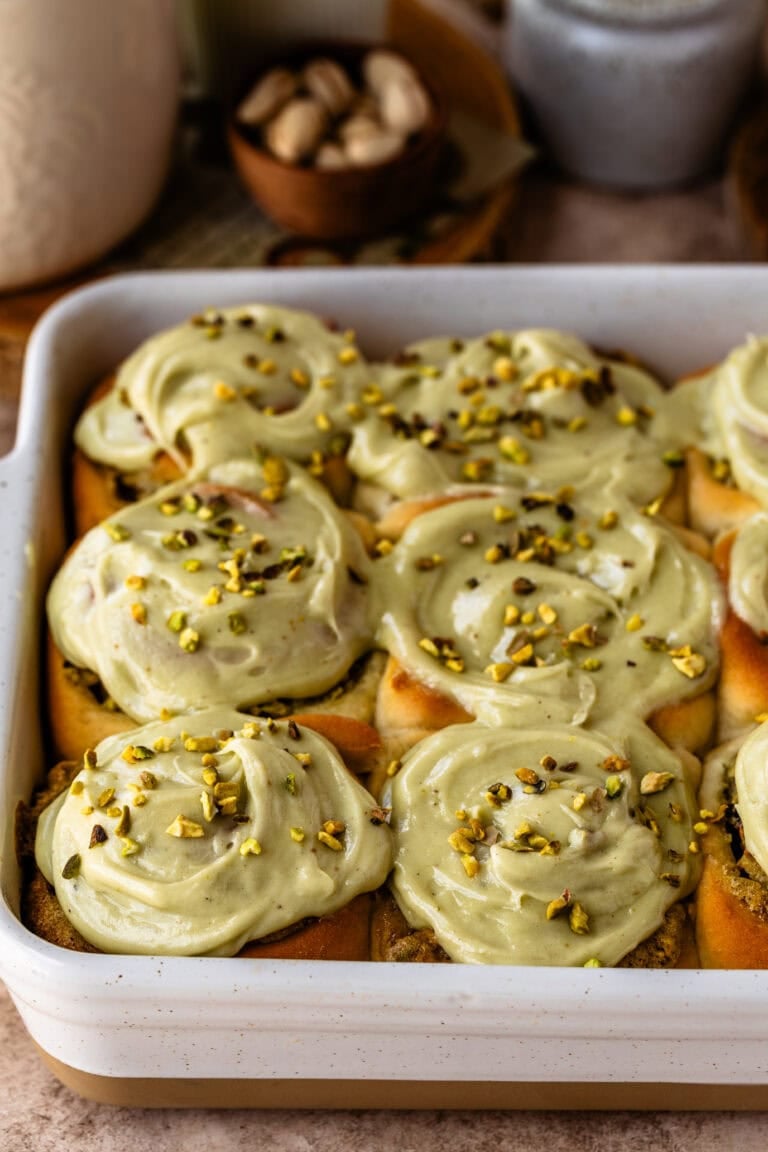 A pan of freshly baked pistachio rolls topped with creamy pistachio frosting and sprinkled with chopped pistachios.