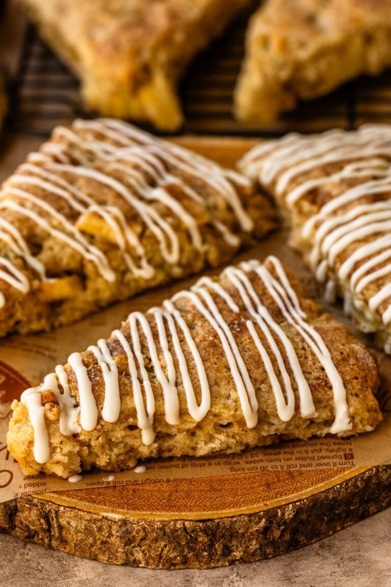 Apple scones arranged on a wooden slice, golden brown with a drizzle of white icing across the tops.