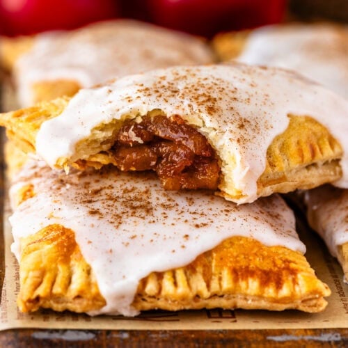 Golden brown apple pop tarts topped with white glaze and sprinkled with cinnamon, with one pastry showing the spiced apple filling inside.