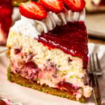 A slice of strawberry cheesecake on a plate, topped with whipped cream, fresh strawberry slices, and strawberry sauce, showing swirls of strawberry filling inside the creamy cheesecake.