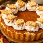 A baked sweet potato pie topped with swirls of whipped cream and decorative leaf-shaped pie crust cutouts, set on a wooden slice.