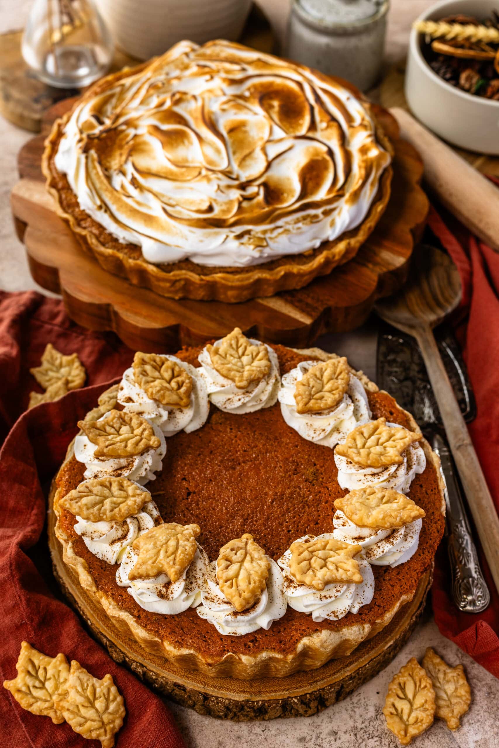 Two sweet potato pies side by side, one topped with toasted marshmallow frosting, the other decorated with whipped cream swirls and leaf-shaped pie crust cutouts.