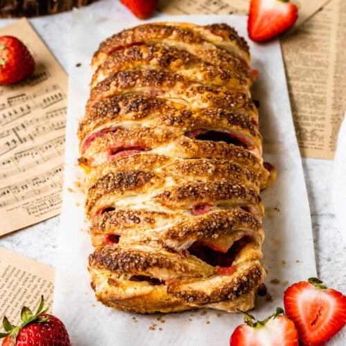 Golden puff pastry braid filled with fresh strawberries and cream cheese, fresh out of the oven on some parchment paper.