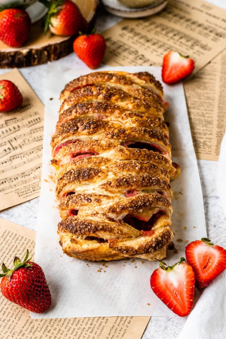 Golden puff pastry braid filled with fresh strawberries and cream cheese, fresh out of the oven on some parchment paper.