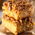 A close-up of two thick pecan pie blondies, showing its gooey pecan topping and dense, buttery blondie layer with bits of pecans throughout.