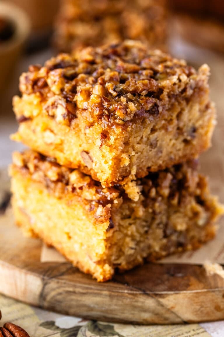 A close-up of two thick pecan pie blondies, showing its gooey pecan topping and dense, buttery blondie layer with bits of pecans throughout.