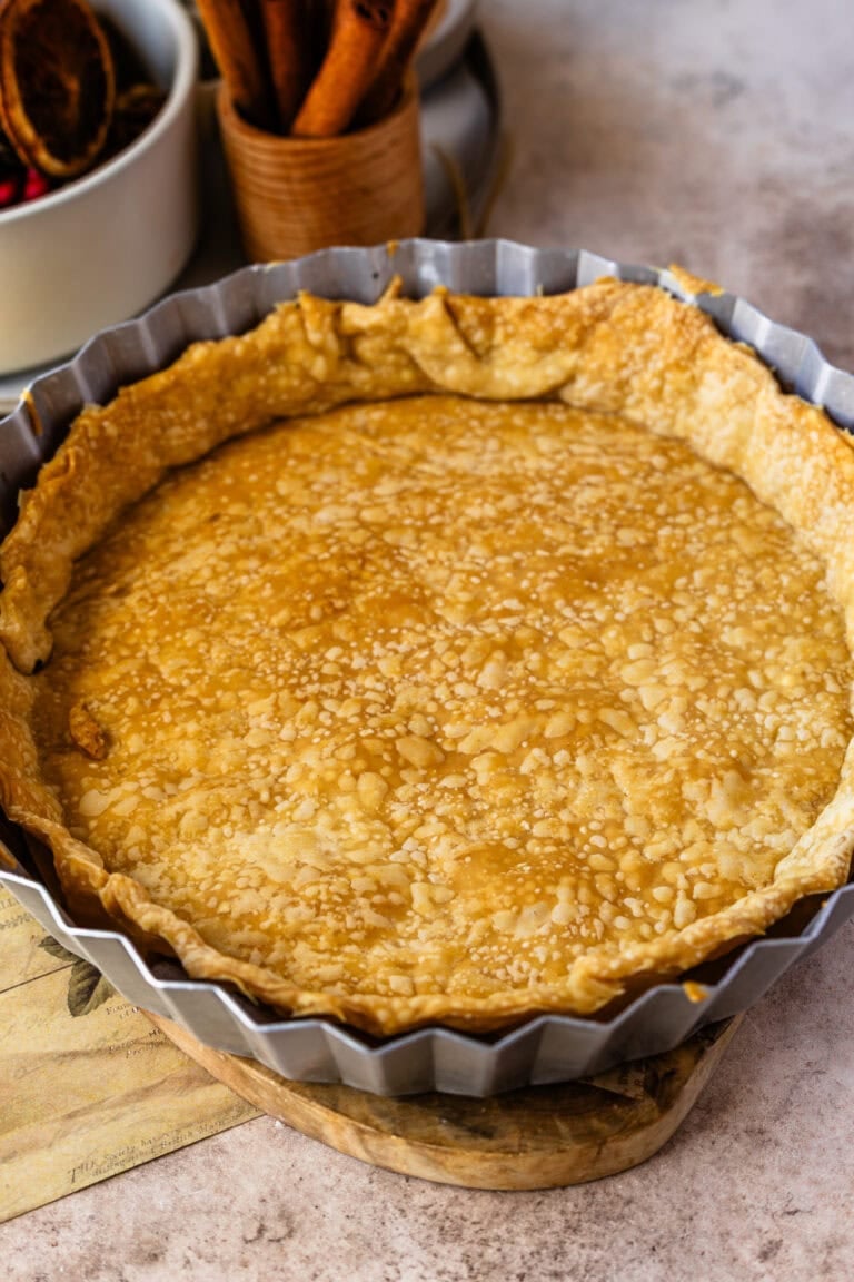A baked pie crust with large bubbles and uneven surface, indicating it wasnโt properly docked or weighted during blind baking. The sides have slightly slumped, and the crust looks patchy rather than evenly flaky.