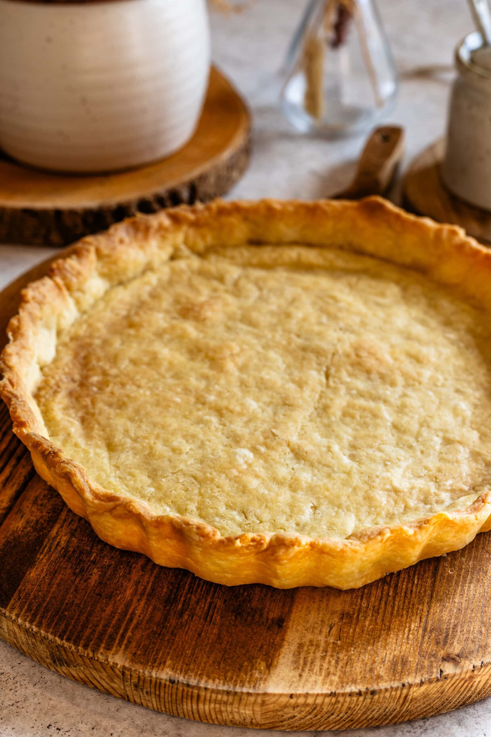A close-up of a golden baked pie crust resting on a wooden board, showing its flaky texture and crimped edges.