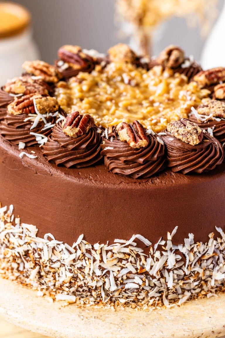 A close-up of the decorated German chocolate cake topped with chocolate swirls, candied pecans, coconut-pecan filling, and toasted coconut around the base.
