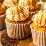 A close-up of frosted salted caramel cupcakes topped with swirls of caramel buttercream and drizzled with golden caramel sauce, arranged together on a rustic surface.