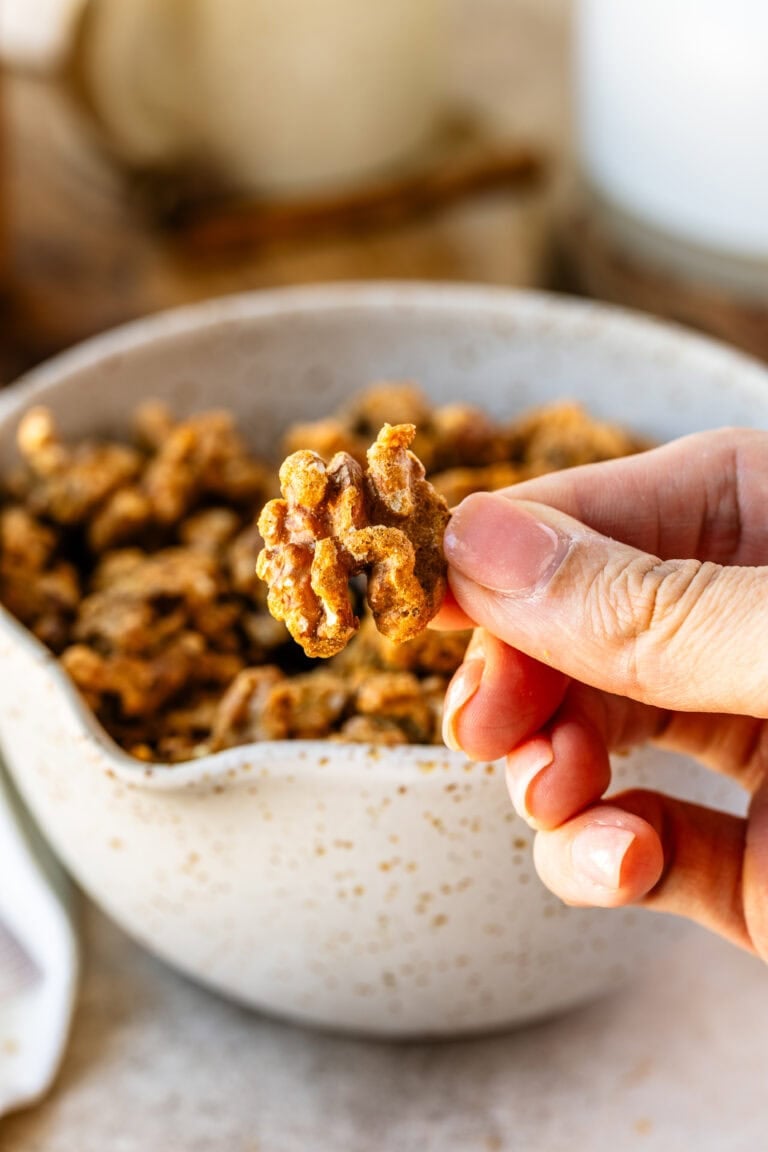 A close up of a hand holding a singular candied walnut.