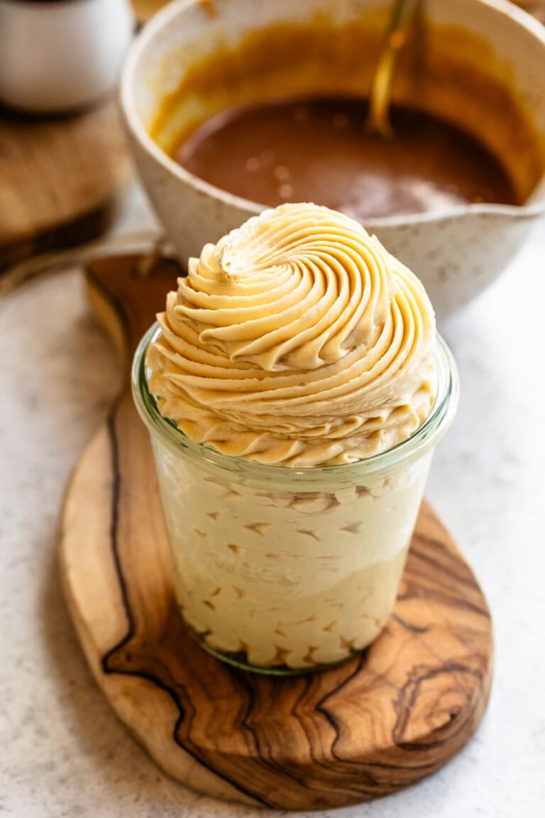 A glass jar filled with silky salted caramel buttercream, topped with a perfect swirl of frosting piped in soft caramel tones.