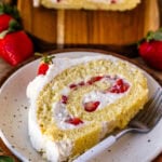 A slice of vanilla Swiss roll cake filled with whipped cream and fresh strawberries on a white plate.