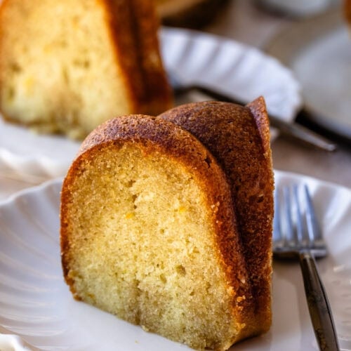 A slice of rum cake on a white plate, showing a moist, golden crumb with a browned exterior.