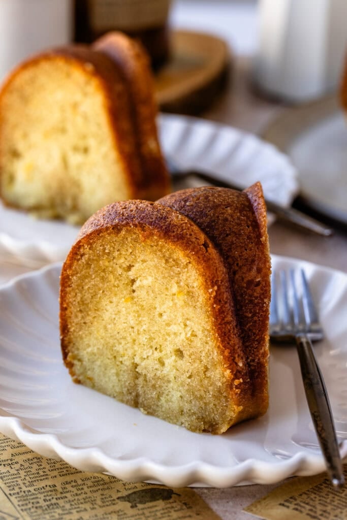 A slice of rum cake on a white plate, showing a moist, golden crumb with a browned exterior.