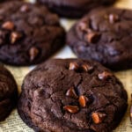 Double chocolate chip cookies stacked on parchment paper, with melted chocolate chips and a soft, fudgy texture.