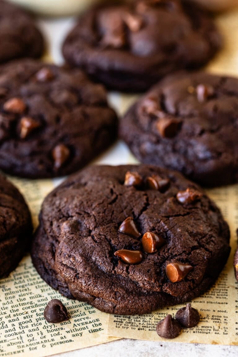 Double chocolate chip cookies stacked on parchment paper, with melted chocolate chips and a soft, fudgy texture.